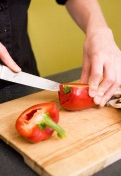 A detail image of a female hand slicing peppers for a pizza.  Shallow depth of field is used to isolate the subject while focus is on the hand cutting the pepper
