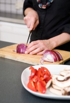 A woman cutting vegetables at home on the counter.  A shallow depth of field is used to bring the hands and red onion in to attention.