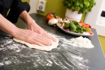 A pair of female hands prepare some bread dough on the counter for pizza.