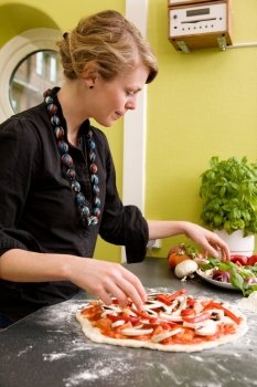 A young female making an italian style pizza at home in her apartment kitchen.