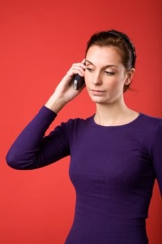 A casual portrait of a brunette caucasian female talking on a cell phone with a red background