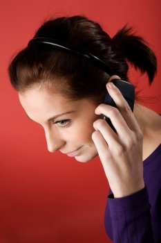 A young female listening on a cell phone. isolated on red.