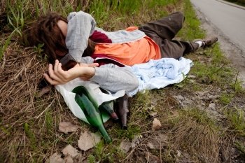 A drunk man laying in the ditch with beer bottles