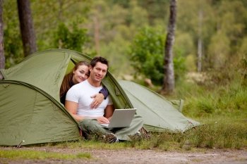 A man and woman using a computer outdoors in a tent