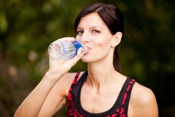 A woman drinking water from a bottle while exercising in a park