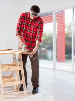 A man in a home interior sanding wood with an electric hand sander