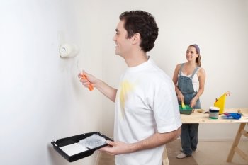 Happy young couple painting the wall white