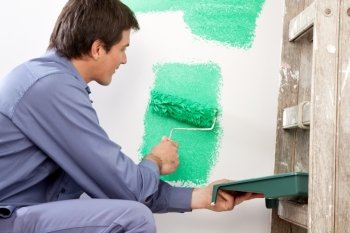 Mature man painting the wall with a roller while holding a paint can