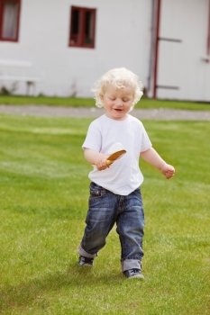 Full length of sweet little boy holding gardening tool in garden and walking