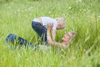 Young pretty woman holding her child while lying on grass