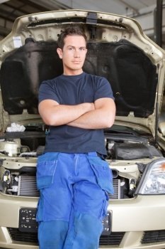 Portrait of a man mechanic leaning against a car looking at the camera