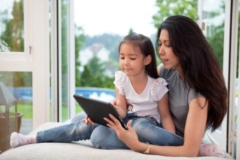Cute little girl sitting with her mother on couch using a digital tablet
