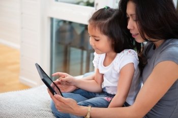 Mother and daughter reading electronic book at home