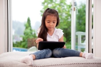 Cute young child using a digital tablet in a home interior with large window