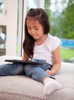 Young girl child looking at a digital tablet sitting on a couch cushion