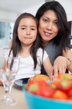 Portrait of mother and her cute daughter sitting at table