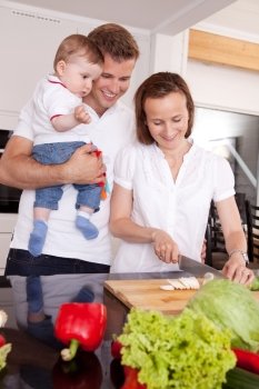 Happy family with mother, father and young toddler son in ktichen preparing food