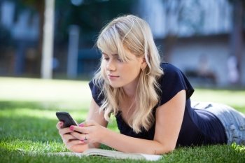 Young college girl using cell phone while lying on grass