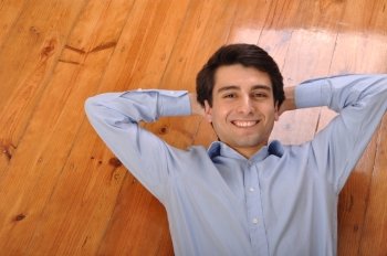 smiling attractive young man lying on wooden floor at home