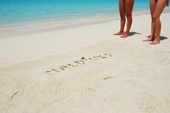 Maldives note written on a white sandy beach with tanned women legs