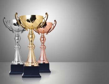 Three trophies, gold, silver and bronze on gray background