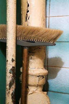 Old broom on a background of sewer pipes and a green wall
