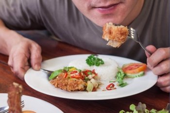 Man eating fried chicken wing and jasmine rice on white plate-meal time