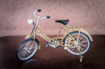 Small gold color toy bicycle on brown leather cushion