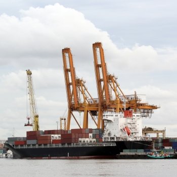 container cargo ship with working crane in shipyard