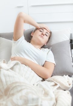 Sick woman taking temperature while lying on bed