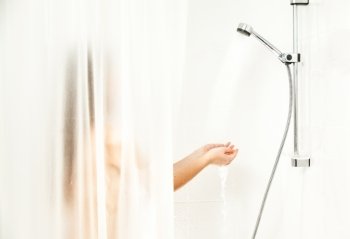 Woman standing behind curtain at shower and holding hands under water