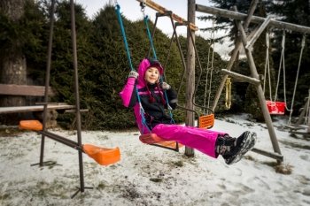 Happy smiling girl riding on swing on playground at snowy day