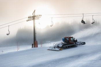 Silhouette photo of snow removal machine working on high ski slope at snowstorm