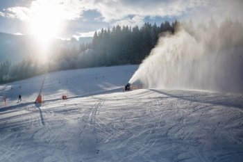 Landscape of snow cannons working on ski slope in Alps at sunny day