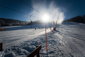 Long fast ski slope with working snow cannons at sunny day