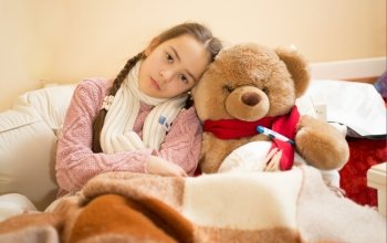 Portrait of sad girl with flu lying in bed with teddy bear
