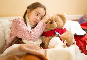 Portrait of little girl hold hand on teddy bears head and measuring temperature