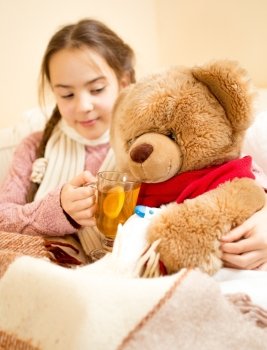 Closeup photo of sick girl lying in bed and giving tea to teddy bear