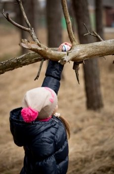 Little girl reaching for Easter egg on high tree branch