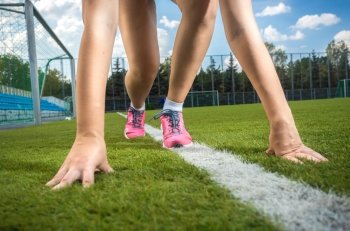 Closeup shot of slim sporty woman getting ready to run on grass track