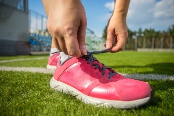 Closeup photo of woman tying up pink sneakers on soccer field