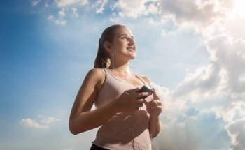 Closeup portrait of beautiful woman listening music while running at sunny day