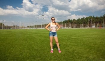Beautiful slim woman standing on soccer field at sunny day