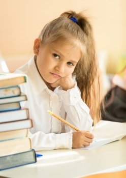 Portrait of upset girl writing test in classroom and looking at camera