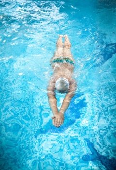Young man in goggles swimming under water at swimming pool