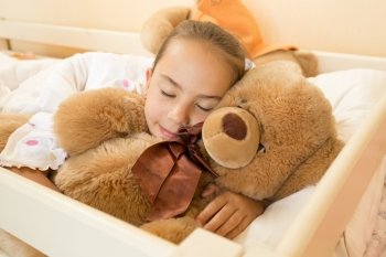 Portrait of little girl sleeping on big teddy bear at bed
