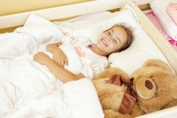 Beautiful smiling girl lying on bed with big teddy bear