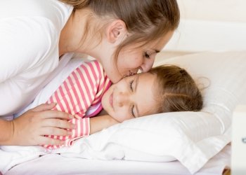Portrait of young mother kissing sleeping daughter at morning
