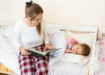 Young mother sitting on bed next to daughter and reading a story