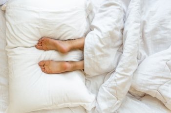 Closeup view of feet lying on soft white pillow at bed
